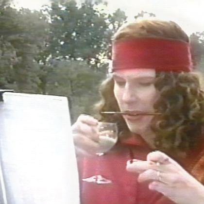 woman with paint brush between teeth looking at artwork on easel