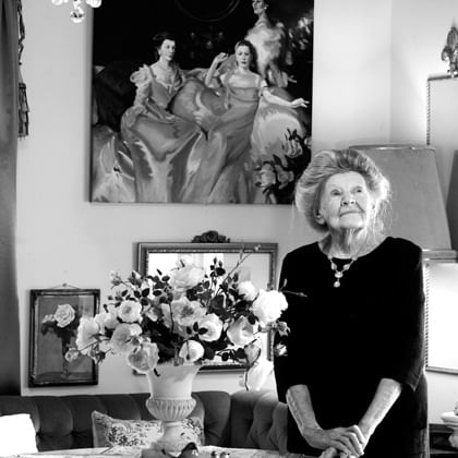 portrait of woman in her sitting room with a vase of flowers on table next to her