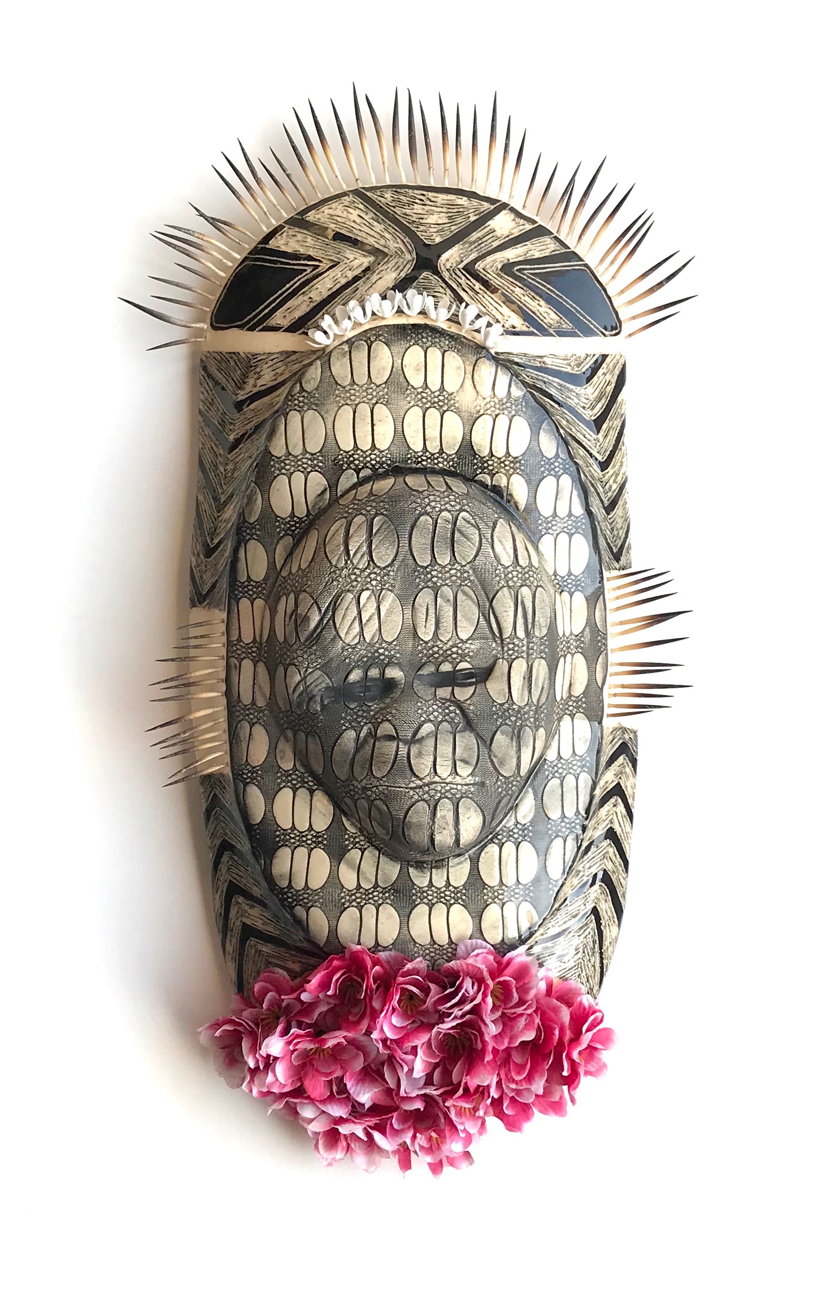 patterned sculpture of shield shape with relief sculpture of person and decorated with echidna quills and flowerss