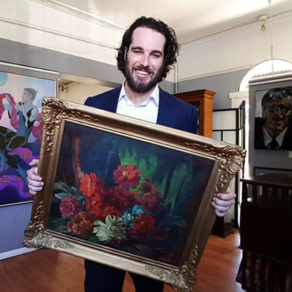 man holding still life painting of roses in a silver frame