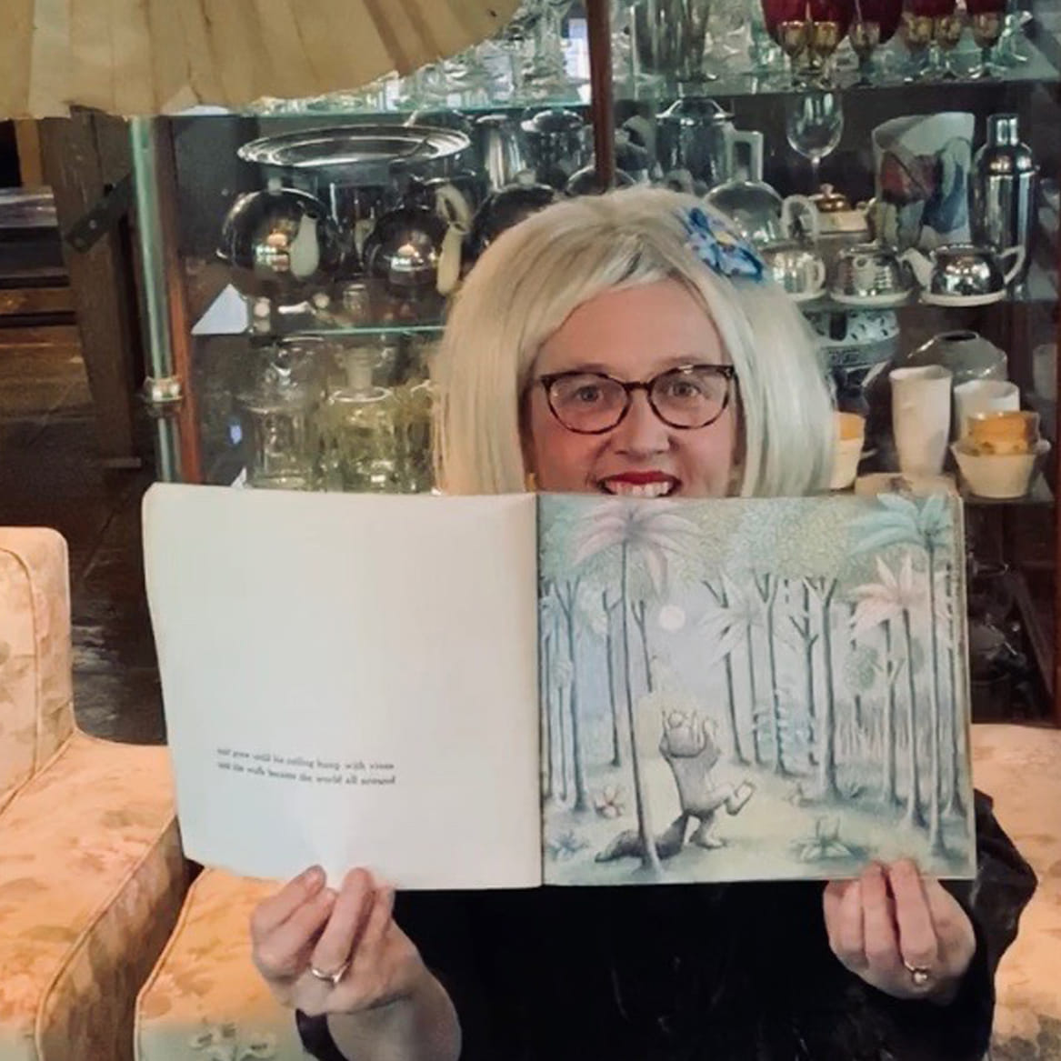 Peggy Pop Art sitting on couch holding open book in front of her 