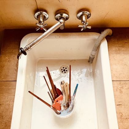 a sink with a container holding multiple paint brushed and other painting tools