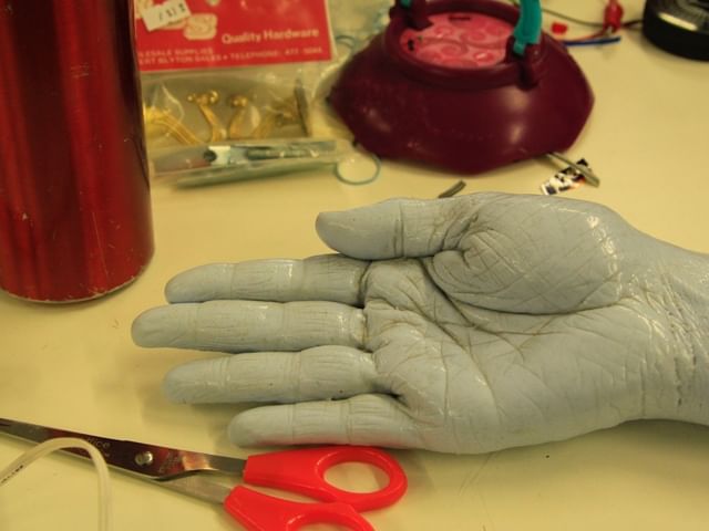 coloured hand surrounded by craft tools including scissors, picture hangers and clamps 