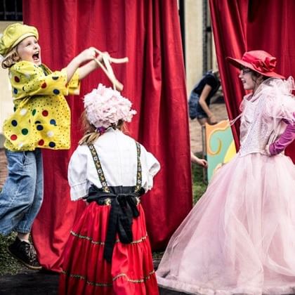 three children in dress-up costumes in front of red curtain 