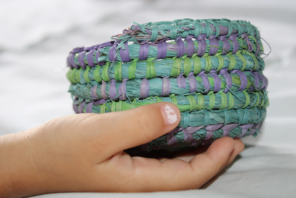 A child's hand holding a colourful woven basket