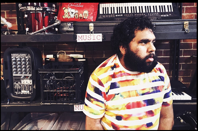 A First Nations man sitting in his music studio surrounded by equipment