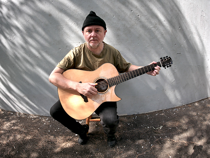 A man squatting on the street playing an acoustic guitar