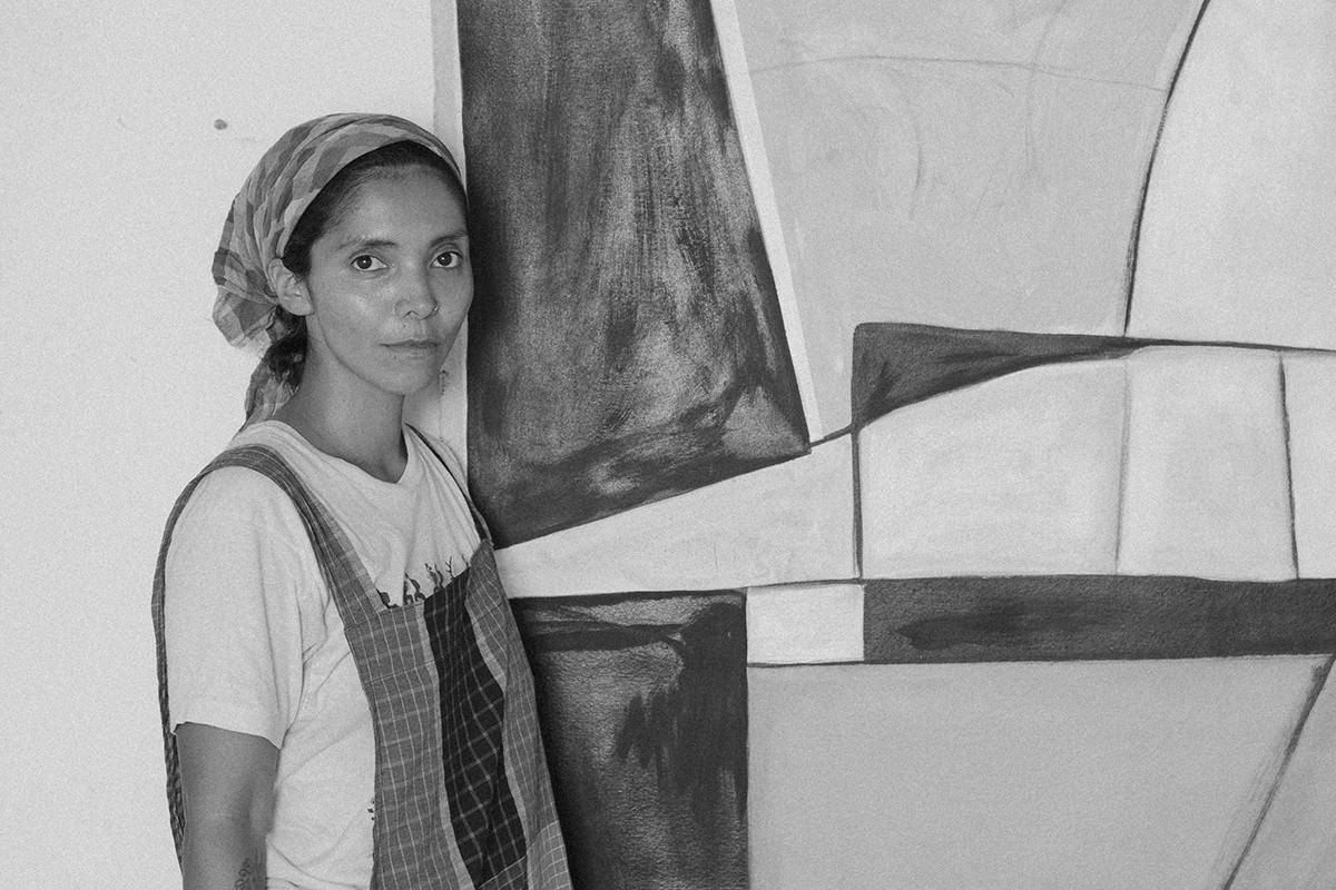 A woman of colour standing in front of her large scale painting