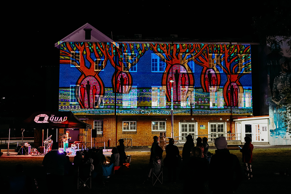 The Lismore City Library at night with a large scale projection of an animation of colourful boab trees.