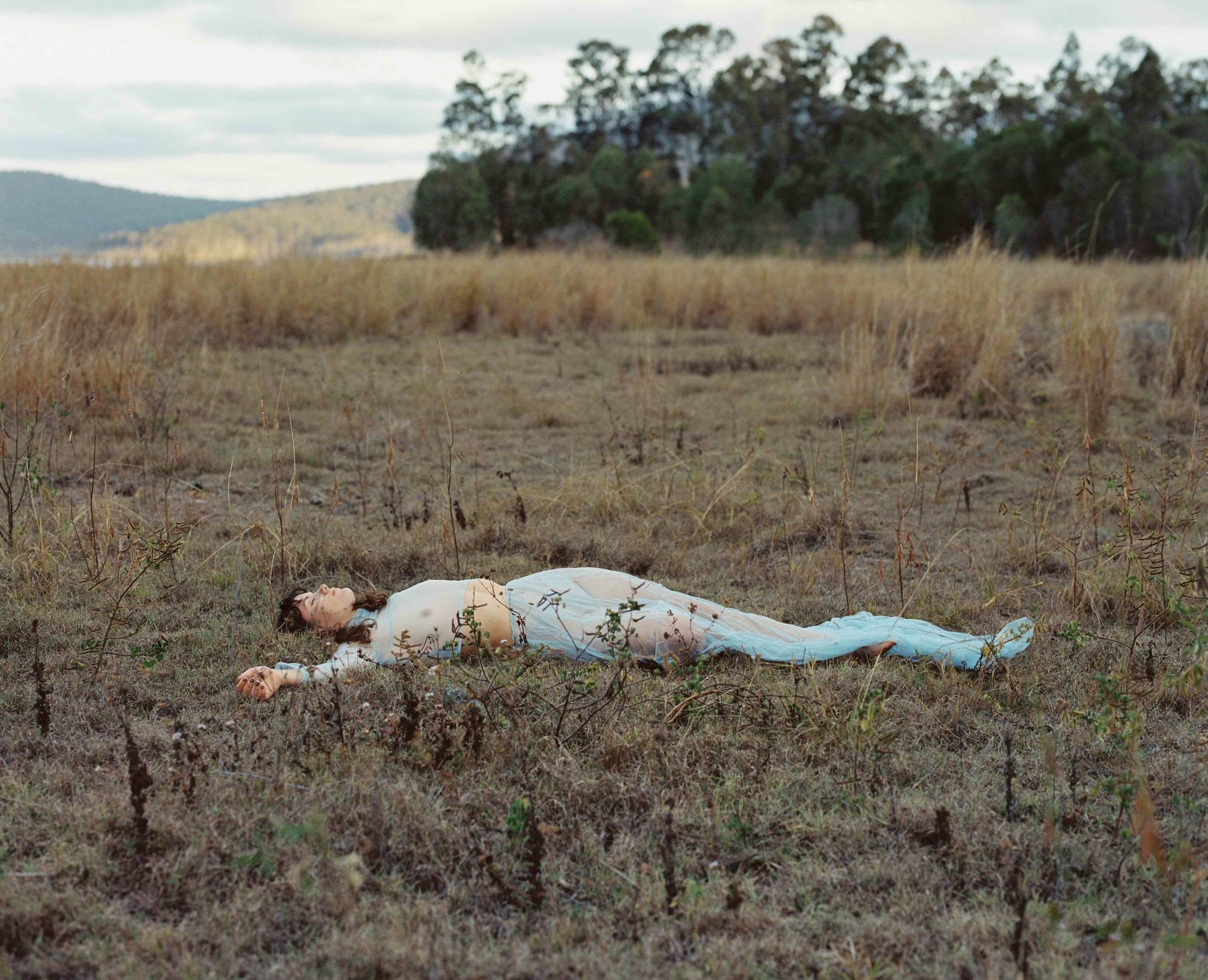A woman wearing light blue lying down in a field of dry grass