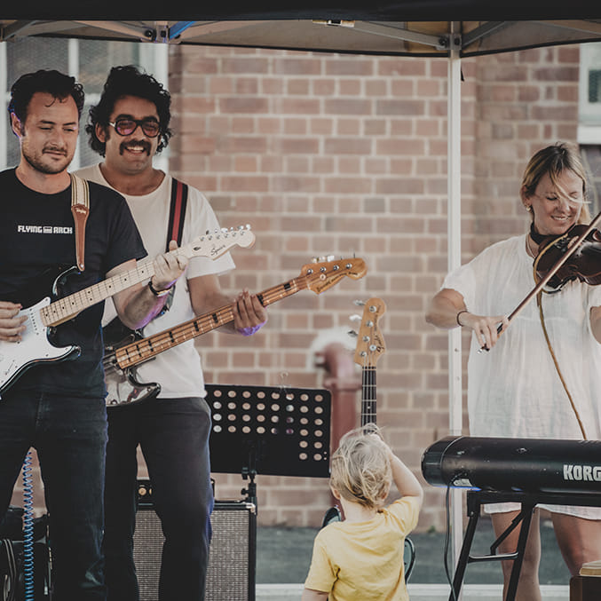 A band playing live, smiling at a young child in the audience