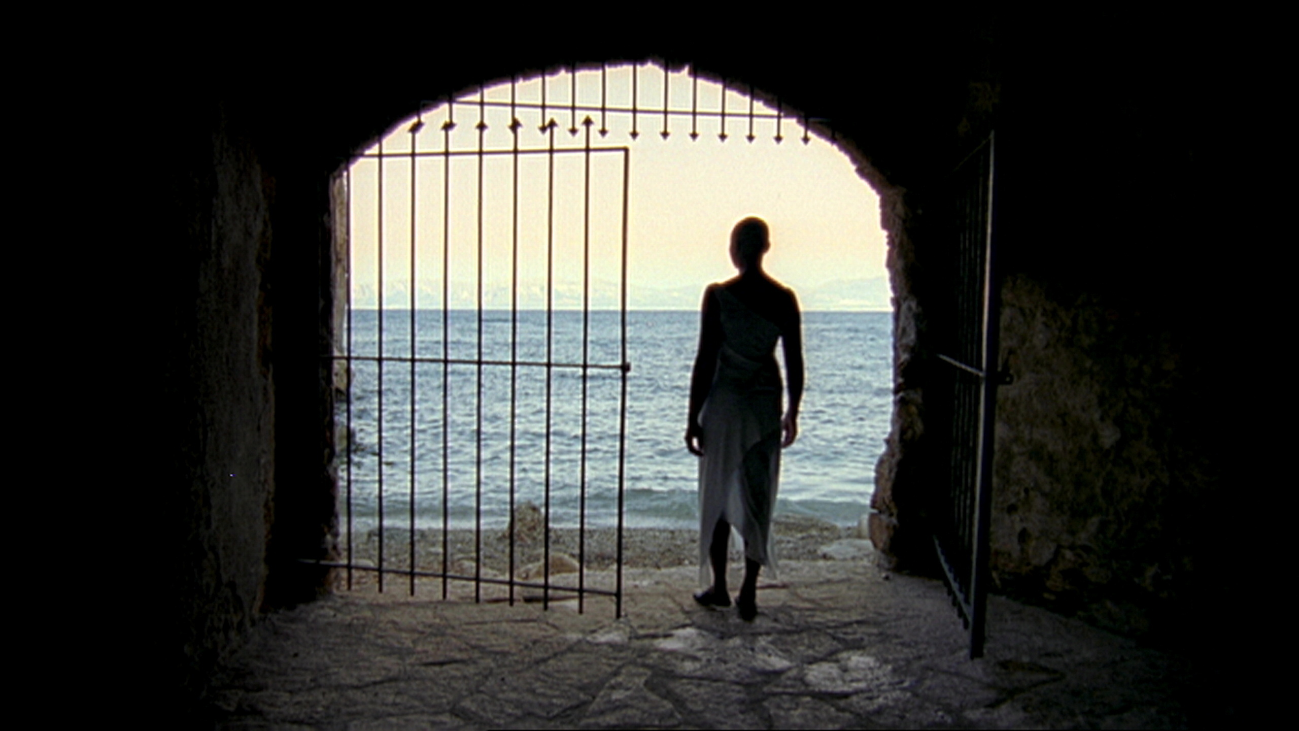 A colour photo of a silouetted figure standing next to a gate in a tunnel with the sea behind them