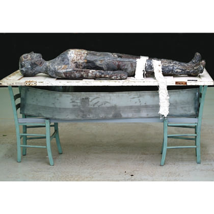 sculpture of body on recycled door, chairs and tin coffin liner