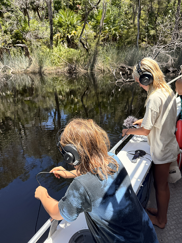 Two youths on a boat with headphones and microphones recording the water