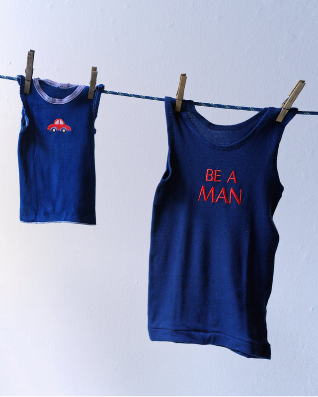 child's singlet with car motif  hanging on clothes line beside men's singlet with 'be a man' caption on front