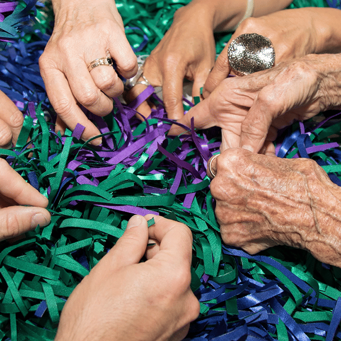hands of multiple people in pile of strips of coloured material