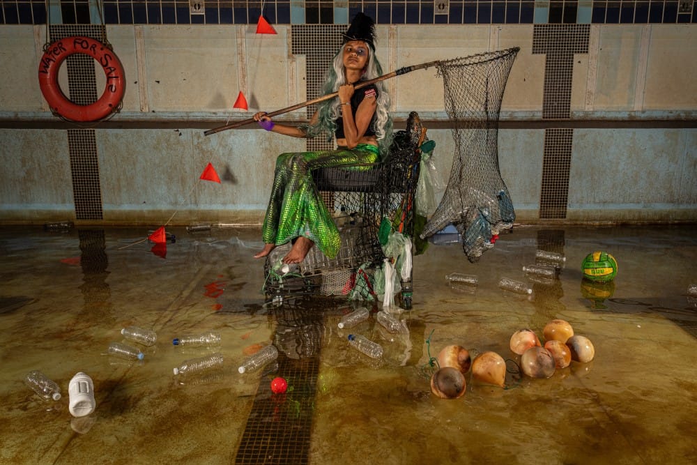 mermaid with fishing net surrounded by rubbish from the seam and some coconuts