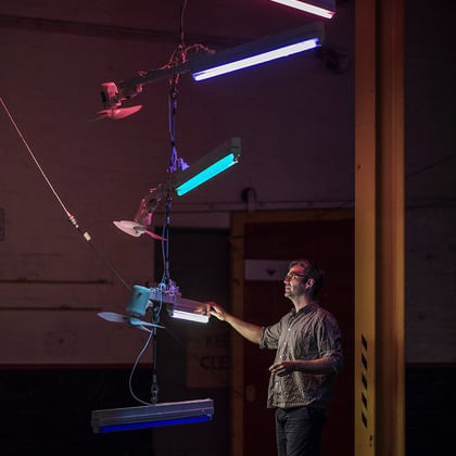 Artist Ross Manning in studio with lights and fans hanging form ceiling 