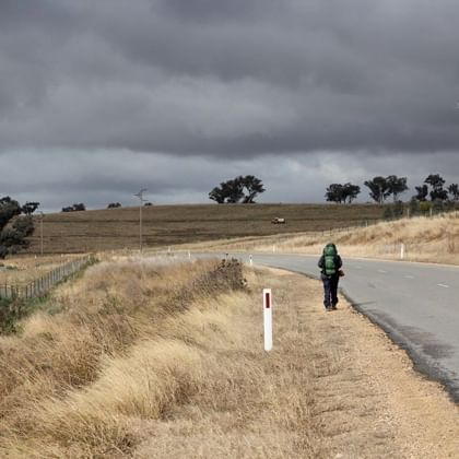 person with backpack on walking down deserted rural road 