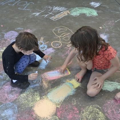 two children doing chalk drawing on the ground 