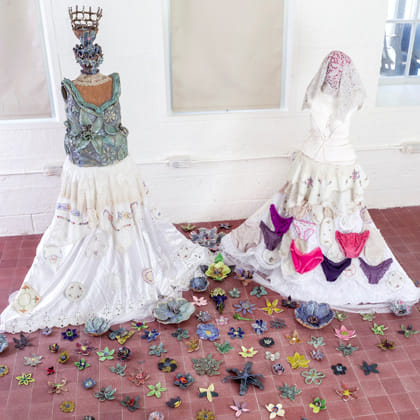 two sculptures of women in skirts surrounded by ceramic flowers on the floor 