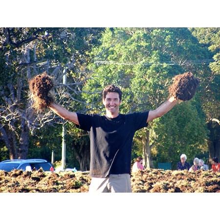 man holding up clumps of soil in front of forest background
