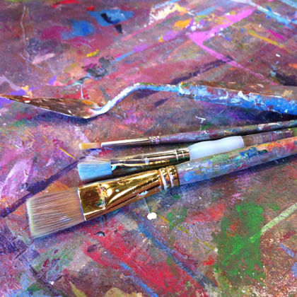 paint brushes on a table with multi coloured paint splotches