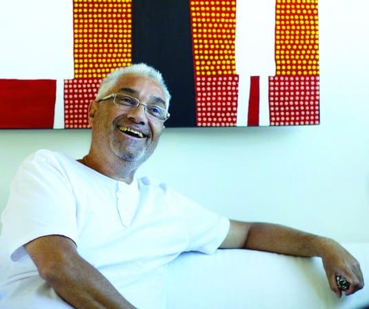 Michael Philp sitting on a couch  in front of one of his colourful paintings 