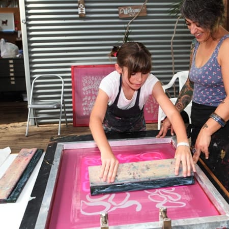 Audrey Bush using squeegy to make sceenprint with Joanna Kambourian looking on 