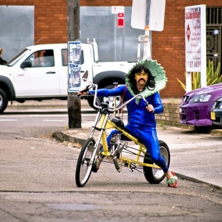 man in blue suit with large green collar siding bike with high handlebars