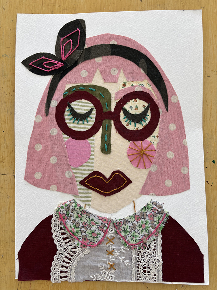 An artwork made from pieces of colurful fabric, creating a portrait of a woman with pink polka dot hair, maroon glasses and a magenta and lace dress