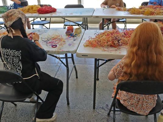 Two youths sitting at a desk creating at a weaving workshop