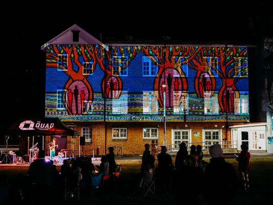 The Lismore City Library at night with a large scale projection of an animation of colourful boab trees.