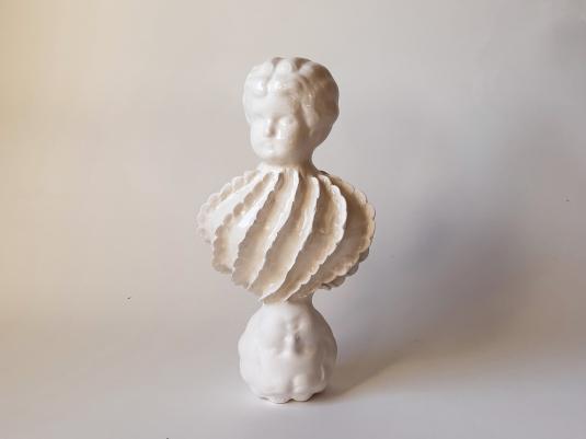 A white ceramic sculpture of two doll heads and a mollusc shape in between