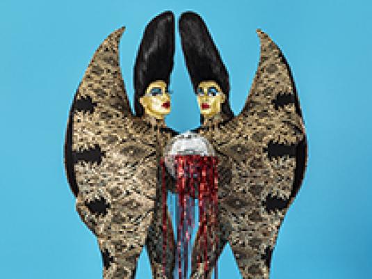 Two figures with gold faces, high 'beehive' hair, and a single set of large wings shared by the two figures.