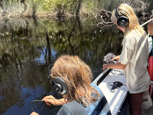 Two youths on a boat with headphones and microphones recording the water