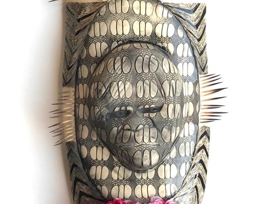 patterned sculpture of shield shape with relief sculpture of person and decorated with echidna quills and flowerss