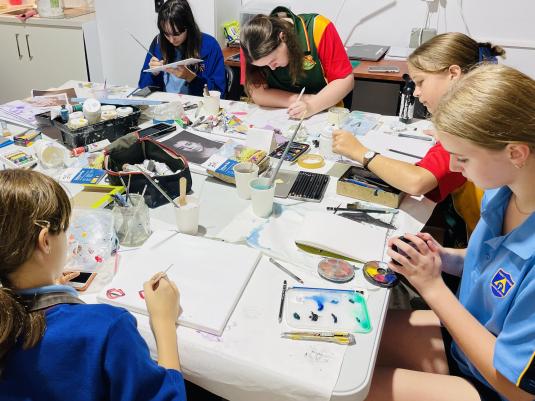 A group of 5 teens in school uniform, sitting around a table making art.