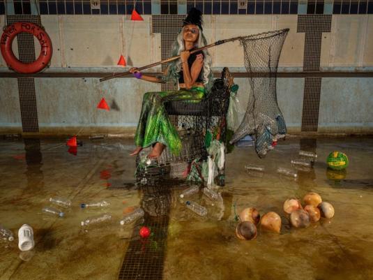 mermaid with fishing net surrounded by rubbish from the seam and some coconuts