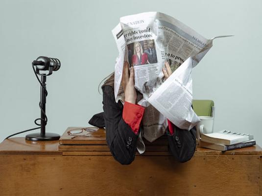 person sitting at news desk with a page from a newspaper wrapped around their head