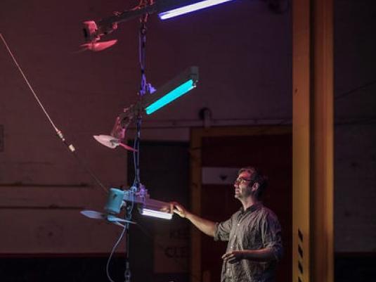 Artist Ross Manning in studio with lights and fans hanging form ceiling