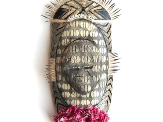 oval shaped ceramic work with relief head shape with patterned glaze over work. There is a bunch of flowes ant the bottom o the piece and decorative echidna quills on the top and side edges.