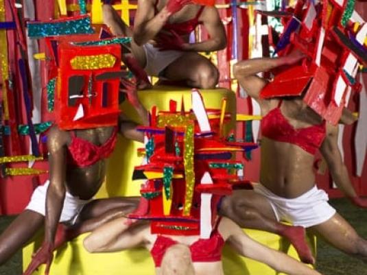 group of people wearing colourful masks and all dressed in white shorts and red bras