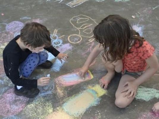 two children doing chalk drawing on the ground