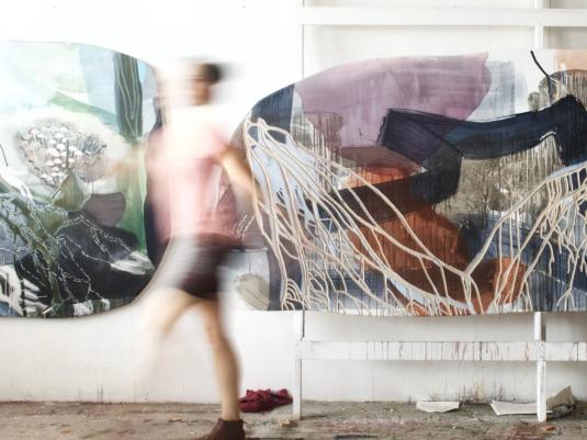 blurred movement shot of Emma Walker in her studio with artworks behind her