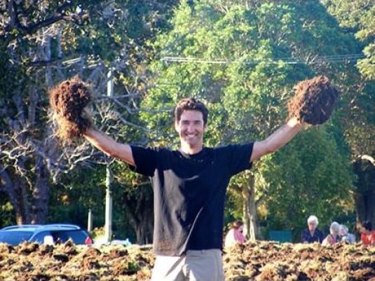 man holding up clumps of soil in front of forest background