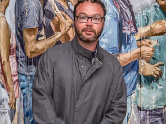 artist Fintan Magee standing in front of is mural of a group of people.