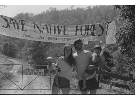 Nan and Hugh Nicholson with their two children on a dirt road with a 'save native forest' banner behind them