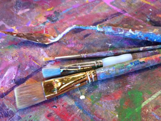 paint brushes on a table with multi coloured paint splotches